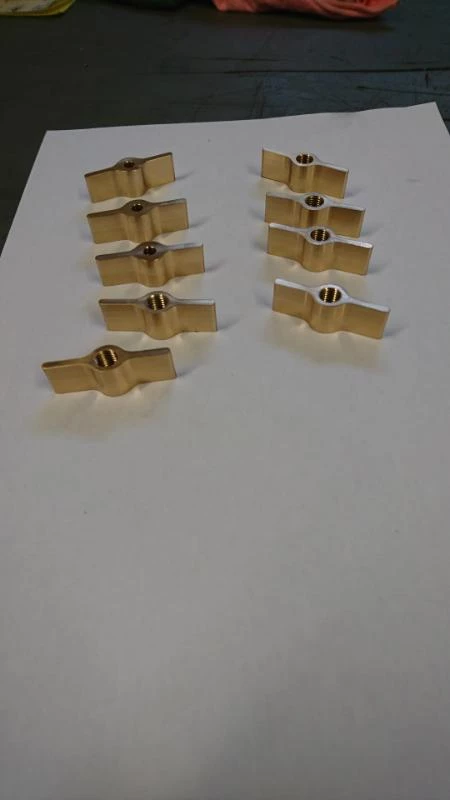 Petites pièces en bronze usinées, alignées sur une feuille blanche